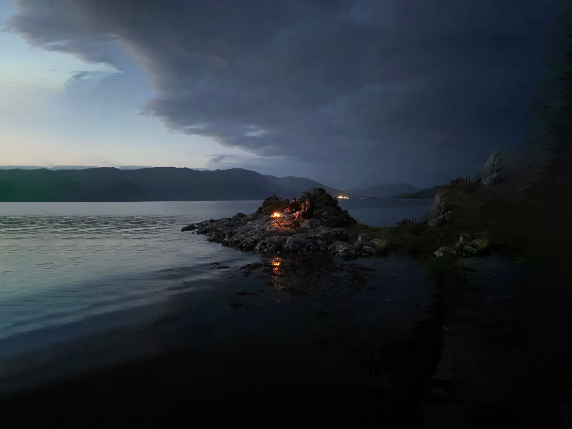 Friends around a fire on a rocky spit at dusk, with Loch Carron and the hills beyond